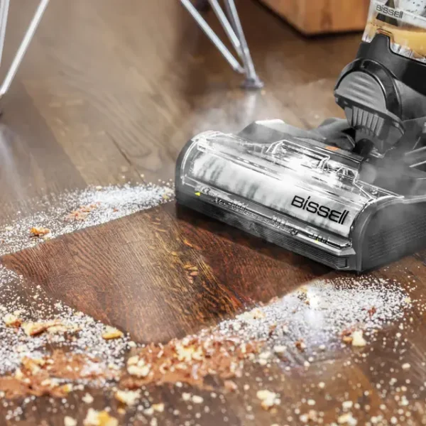 برس جلوی جارو و زمین شوی بخاری بیسل CrossWave HydroSteam روی کف چوبی تیره، با بخار آب و خردهریز روی زمین